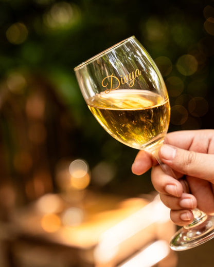 Personalized wine glass with gold 'Diya' engraving, held with a golden drink