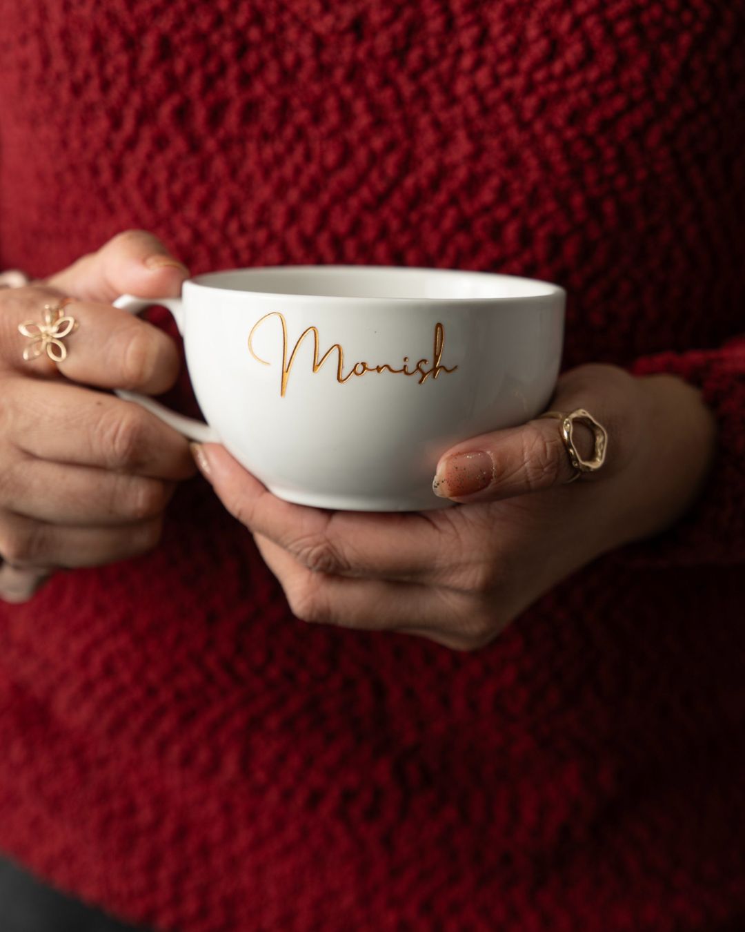 Weiße Keramiktasse mit Gravur „Monish“ in Goldschrift, von zwei Händen gehalten