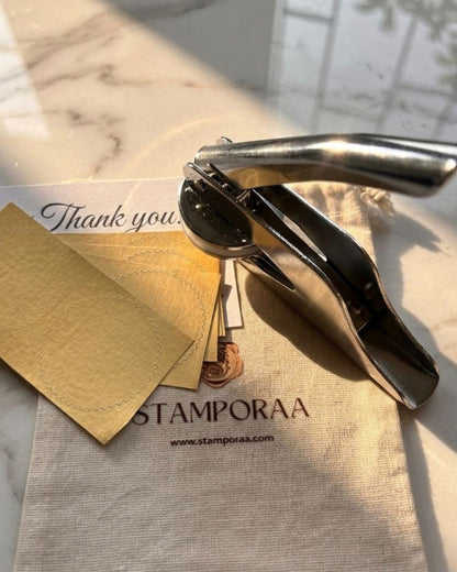 Metal paper embosser stamping 'Thank you!' on beige paper card