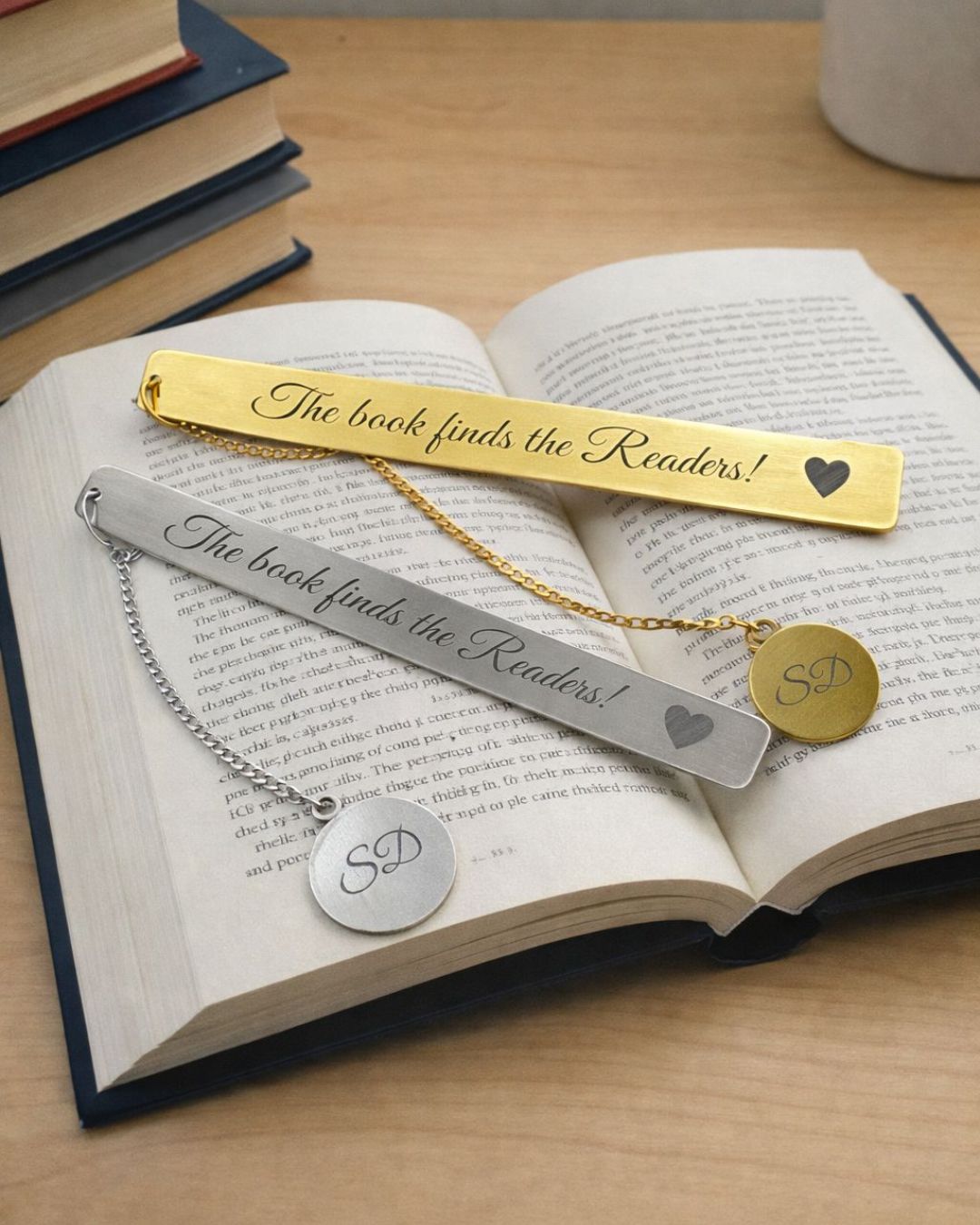 Gold metal bookmark with heart and cursive “The book finds the Readers!” plus round “SD” tag