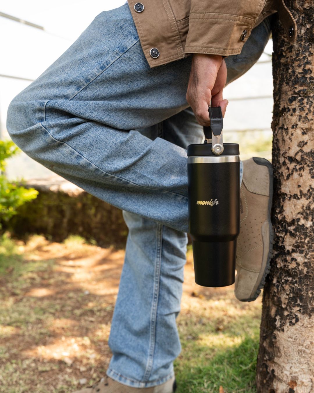 Black steel tumbler with lid and carry strap, held in hand
