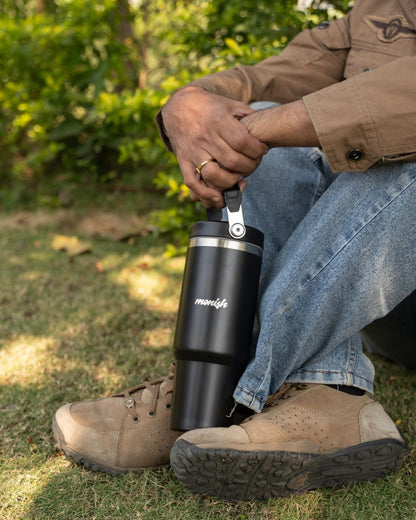 Black steel tumbler with flip lid and carry handle, outdoors on grass