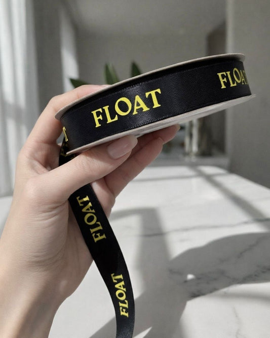 Schwarzes Satinband mit goldenem „FLOAT“-Schriftzug, gerollt auf Spule