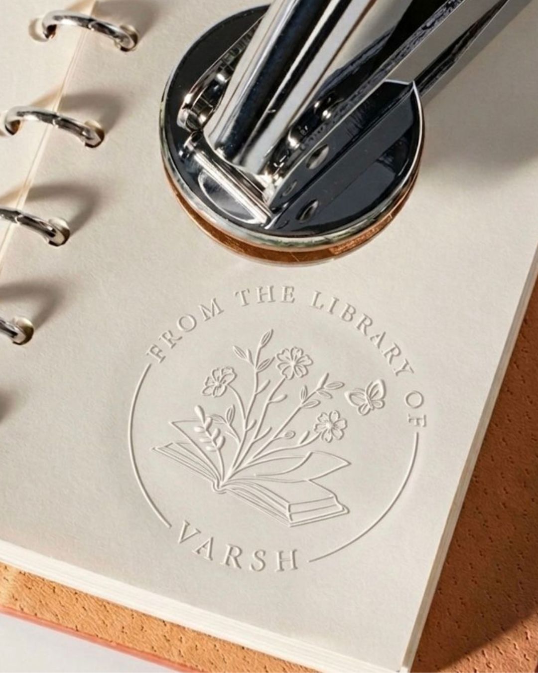 Floral library embossing seal on paper with book icon; embossing head above